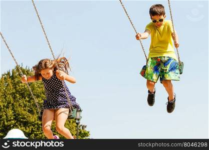 Two children having fun on swingset.. Fun and joy of children. Little girl and boy playing outdoor on preschool playground garden. Kids swinging on swing-set to touch the sky.