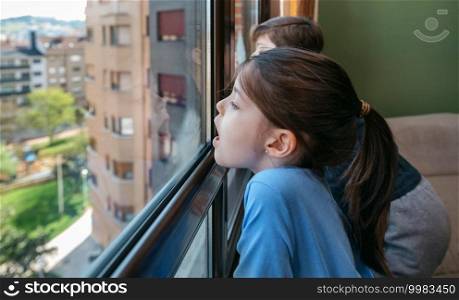 Two children in coronavirus lockdown playing breath on the glass as they look through the window