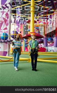 Two children in helmets climb on zip line in entertainment center, young climbers, front view. Boy and girl having fun on ropes in climbing area, kids spend the weekend on playground, happy childhood. Children in helmets, young climbers, front view