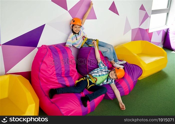 Two children in helmets relaxing in climbing area in entertainment center, young climbers. Boy and girl having fun on ropes, kids spend the weekend on playground, happy childhood. Children in helmets relaxing, young climbers