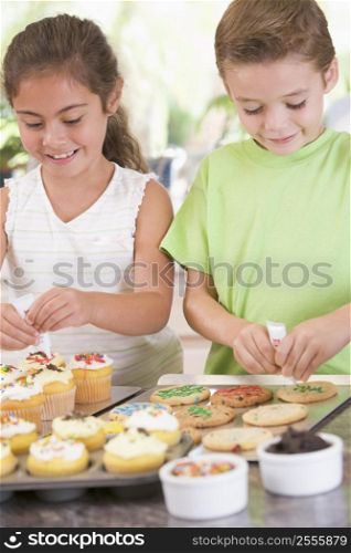 Two children in kitchen decorating cookies smiling
