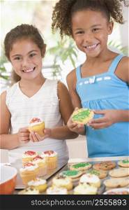 Two children in kitchen decorating cookies smiling