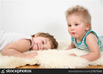 two children lie on fur carpet