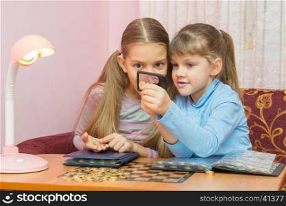 Two children looking at a coin through a magnifying glass