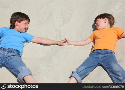 Two children lying nearby on sand look on each other