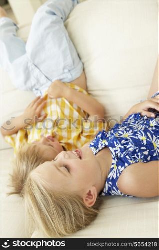 Two Children Lying Upside Down On Sofa At Home