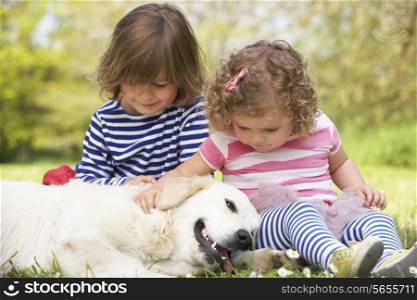 Two Children Petting Family Dog In Summer Field