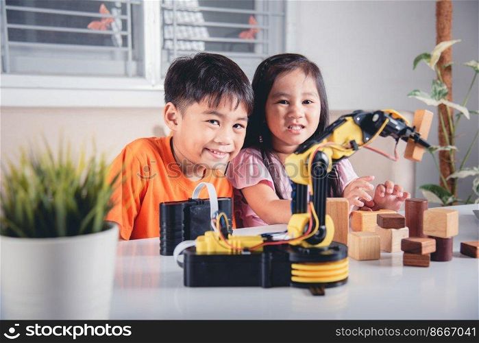 Two children programming and testing robot arm their science, Kid little girl program code to robot with laptop computer and the boy test with remote control to pick up wood block, education lesson