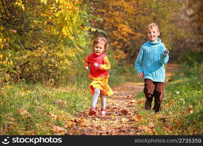 Two children run on wood autumn footpath