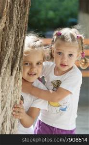 Two children, sisters, simultaneously looked out from behind a tree with one hand