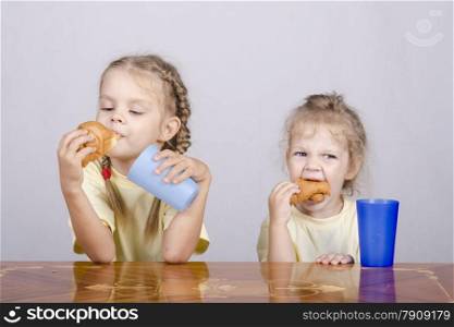 Two children sitting at the table, eating a muffin and drink of colored plastic cups