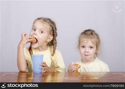 Two children sitting at the table, eating a muffin and drink of colored plastic cups