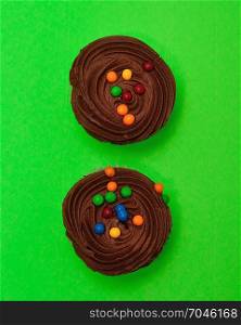Two chocolate cupcakes isolated on a green background