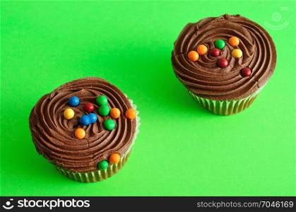 Two chocolate cupcakes isolated on a green background