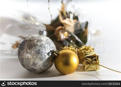 Two Christmas balls and a few little gifts with a white background, golden and silver chistmas balls out of glass, one with ornaments