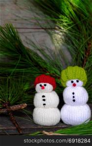 two Christmas snowman from knitted toy standing front of pine