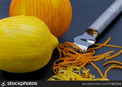 two citrus fruits on a slate plate with zest peeler and strips of peel