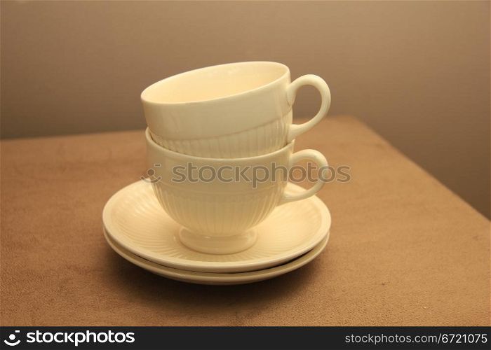 Two classic white teacups, stacked on a beige hocker
