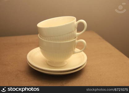 Two classic white teacups, stacked on a beige hocker