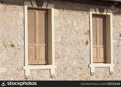 Two closed wooden windows on stone house wall