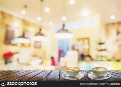 Two coffee cups on brown wooden table over blurred photo of beautiful coffee shop for background use