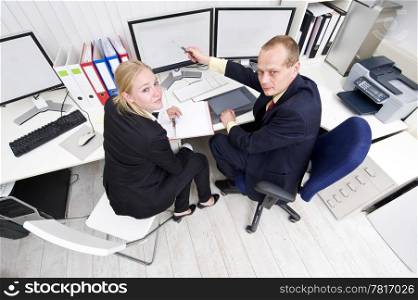 Two colleagues cooperating behind a dual flatscreen monitor