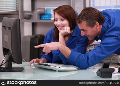 two colleagues in blue jumpsuit watching a computer