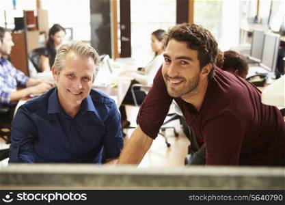 Two Colleagues Working At Desk With Meeting In Background
