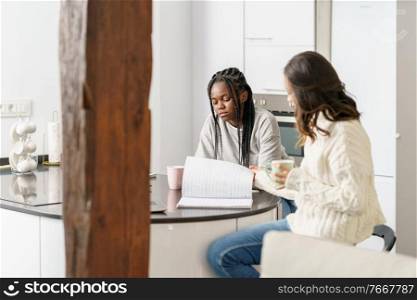 Two college girls studying together at home while drinking coffee. Multiethnic women.. Two college girls studying together at home while drinking coffee