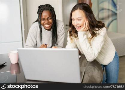 Two college girls studying together at home with laptops while drinking coffee. Multiethnic women.. Two college girls studying together at home with laptops while drinking coffee