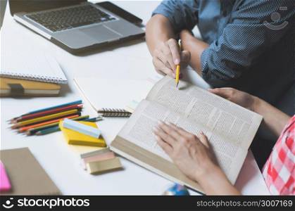 Two college students reading a book or doing homework together at a class or home