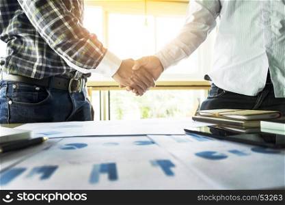 Two confident businessmen handshaking and smiling while sitting at the table together.