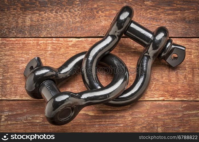 two connected heavy duty shackle (d-ring) for vehicle recovery and towing on rustic red painted wood - strong link or connection concept