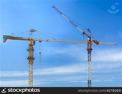 Two construction cranes opposite blue sky