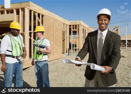 Two construction workers and surveyor holding blueprint
