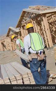 Two construction workers carrying wooden plank on site