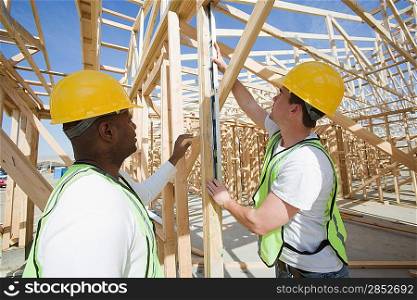 Two construction workers measuring building framework