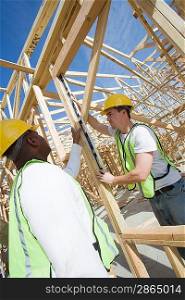 Two construction workers measuring building framework