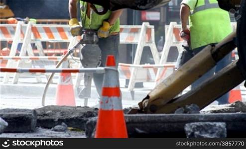 Two construction workers operating jackhammers on a city street