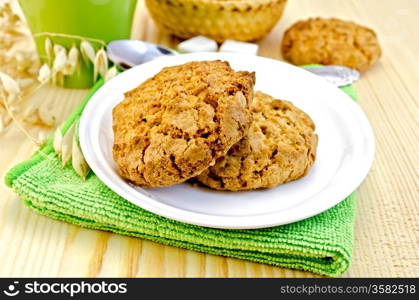 Two cookies on a white plate, spoon, sugar, cup, basket weaving, stalks of oats on a wooden board