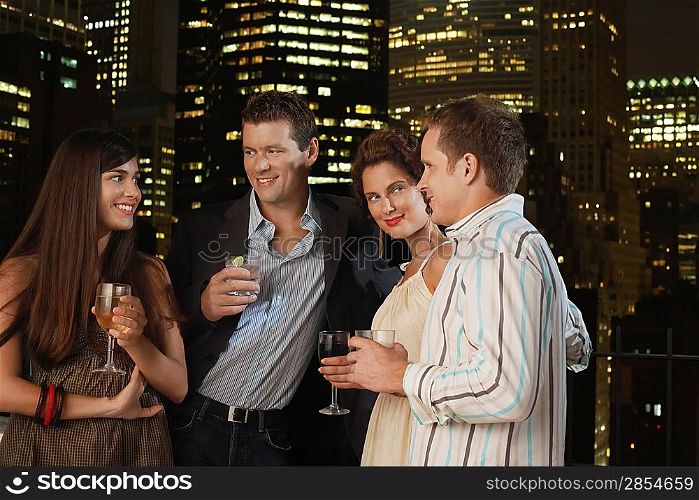 Two couples drinking together against night city skyline