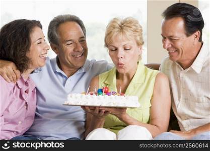 Two couples in living room smiling with woman blowing out candles on cake
