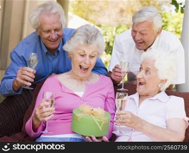 Two couples on patio with champagne and gift smiling