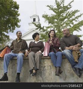 Two couples sitting on a wall and smiling