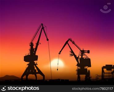 Two cranes sit dramatically against a colorful sunset in a large shipyard
