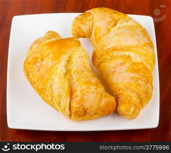 Two croissants on an elegant white plate, over wooden background