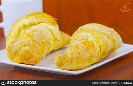 Two croissants on an elegant white plate, over wooden background