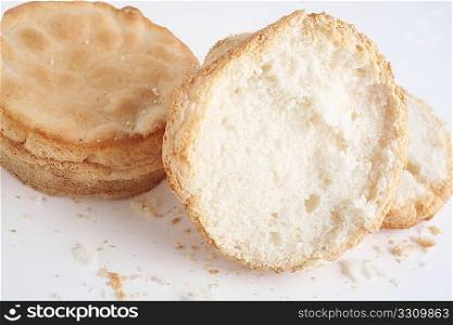 Two crumbly, gluten-free bread rolls, one sliced, over a white background