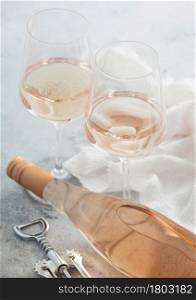 Two crystal glasses and bottle of pink rose homemade wine with steel corkscrew on light table background.