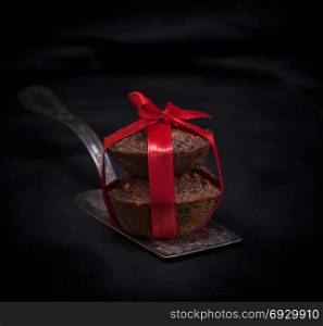 Two cupcakes are tied with a red ribbon on an iron shovel